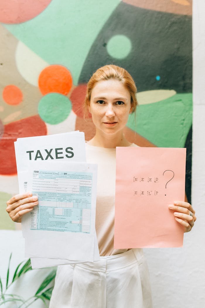 A professional woman holding tax documents and a Need Help? sign, offering tax assistance.